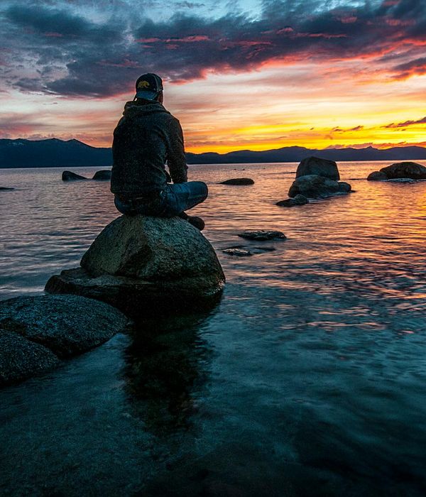 Silhouette of a person meditating at sunset with calm water.